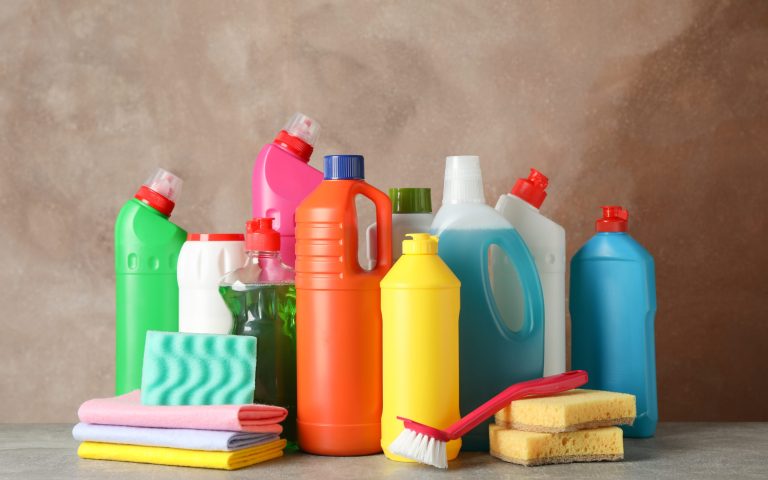Bottles with detergent and cleaning supplies on brown background, space for text